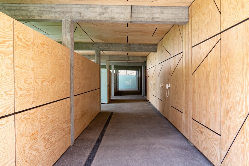 Flurbereich, Decken und Wände mit hellen Holzplatten, Betonverstrebungen, dunkler Boden