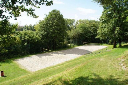 Sandplatz mit gespannten Netzen, gesäumt von grüner Wiese und grünbelaubten Bäumen