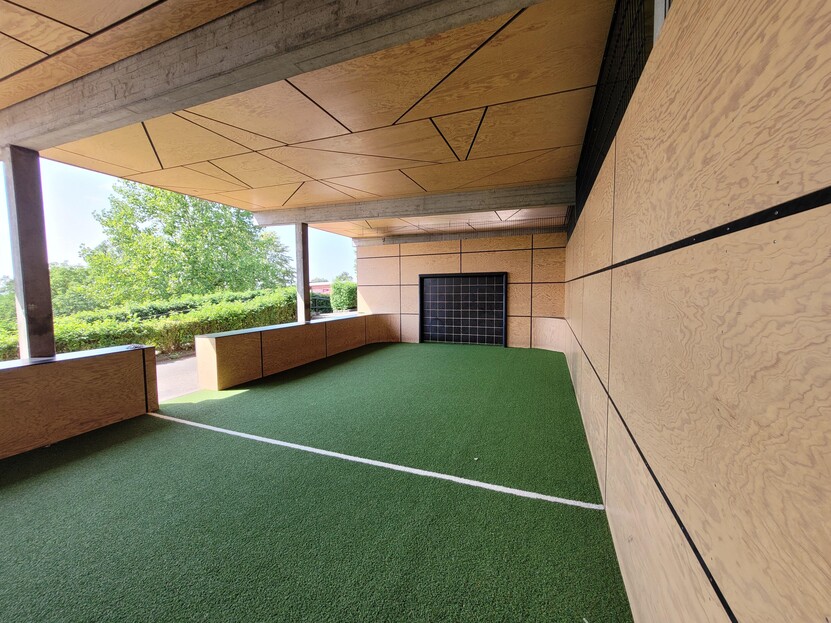 überdachter Soccer-Court, grüner Bodenbelag, schwarze Tore, Begrenzungen und Decke mit hellem Holz verkleidet