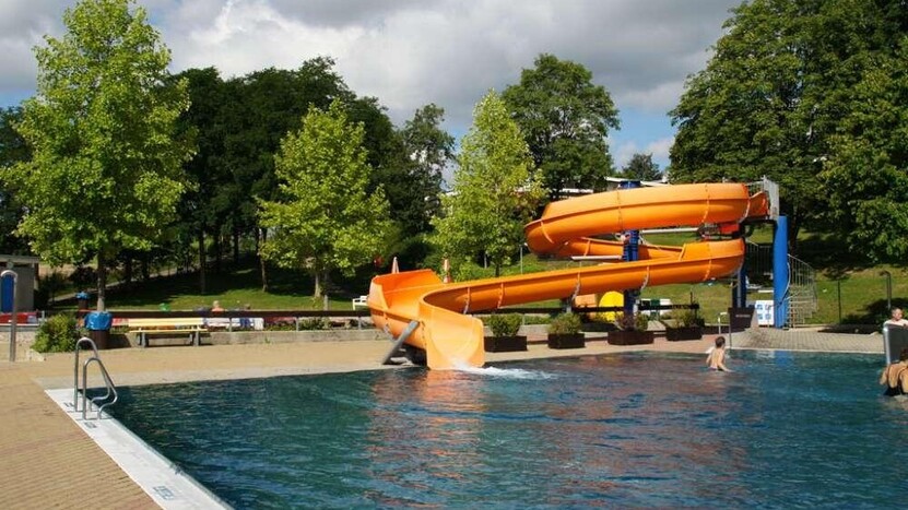 Orangefarbene Rutsche im Nichtschwimmerbecken, Wasser scheint dunkel, Himmel bewölkt