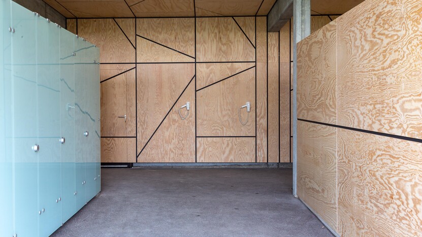 Umkleidekabinen mit Milchglas, Decken und Wände mit hellen Holzplatten, Betonverstrebungen, dunkler Boden
