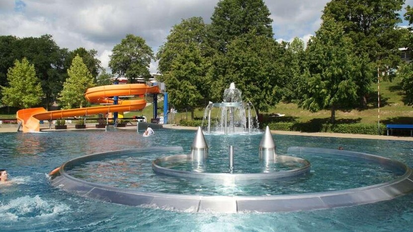 Blick auf die Attraktionen im Nichtschwimmerbecken, Strömungskanal, Wasserkaskade und orangefarbene Rutsche im Hintergrund